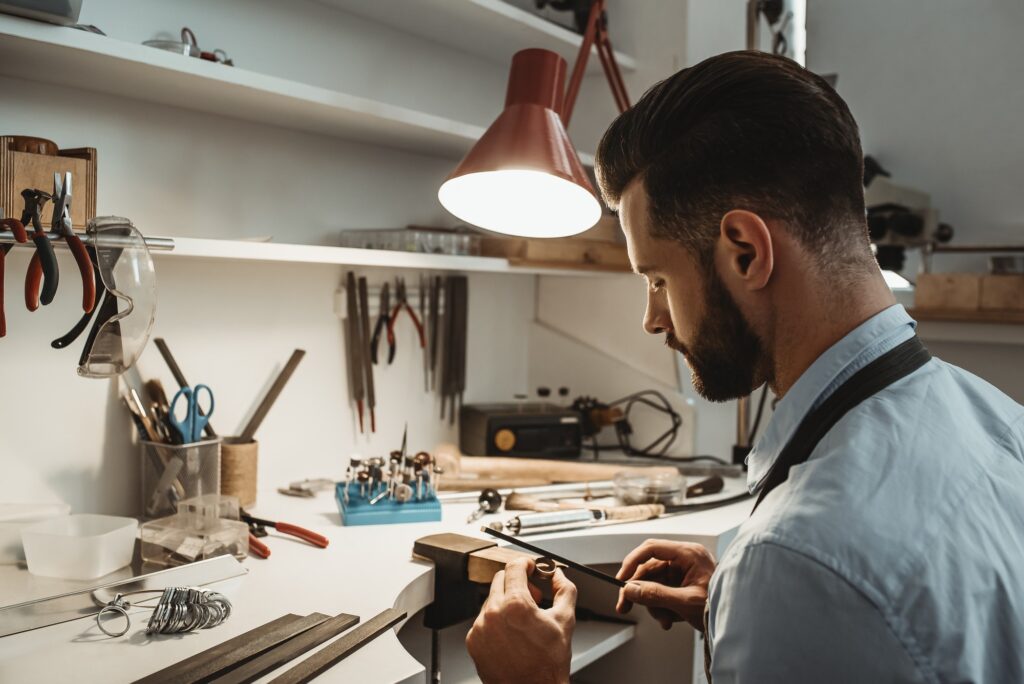 A lot of work in the workshop. Close up of a young male jeweler working and shaping an unfinished