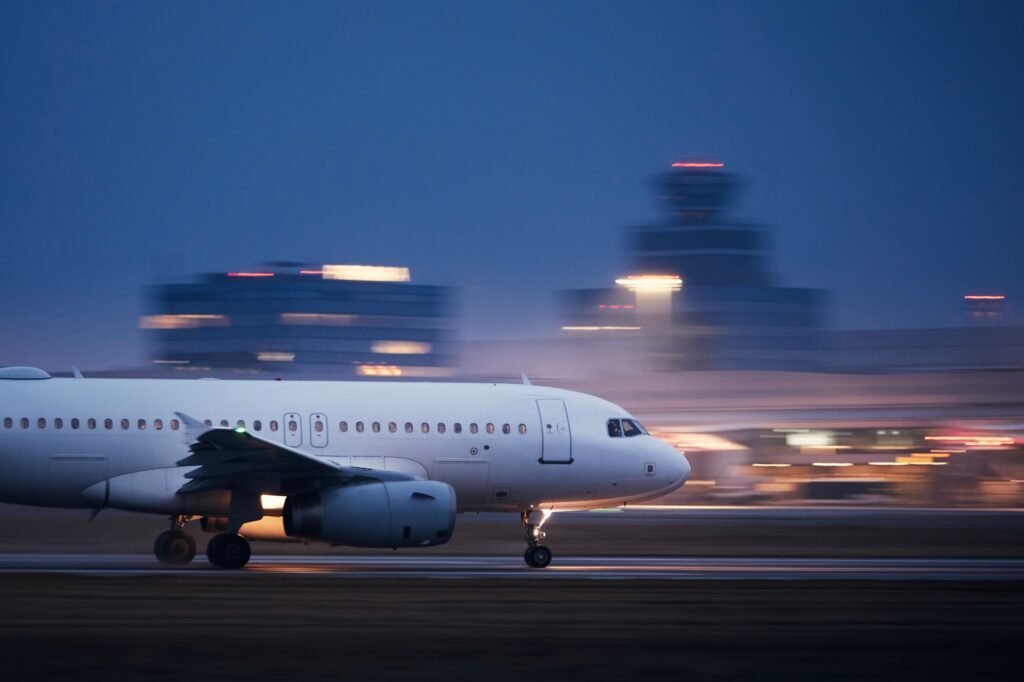 Airplane during take off on airport runway at night against air traffic control tower.