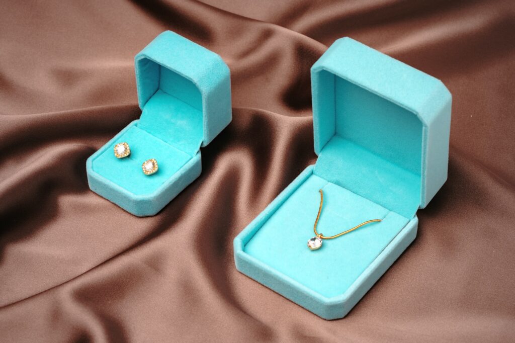 Golden necklace and earrings in blue jewelry boxes on brown silk background