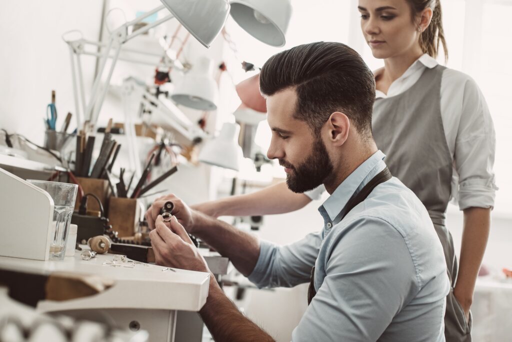 I'll help you. Close-up portrait of young male assistant polishing a ring while female jeweler