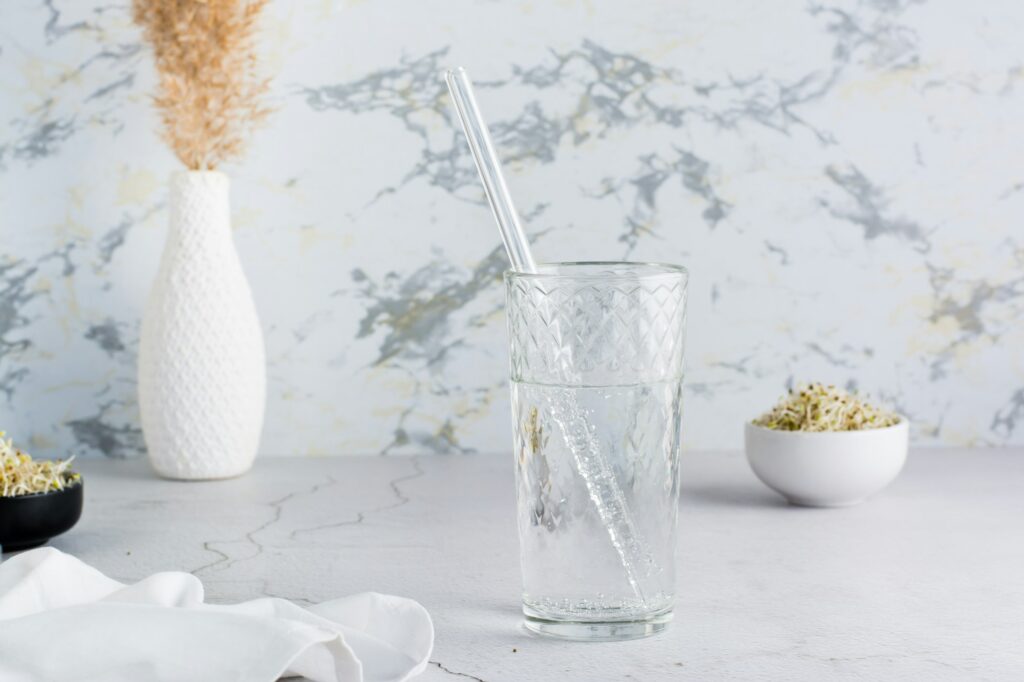 A glass of clean water and a glass straw for drinking on a light table.