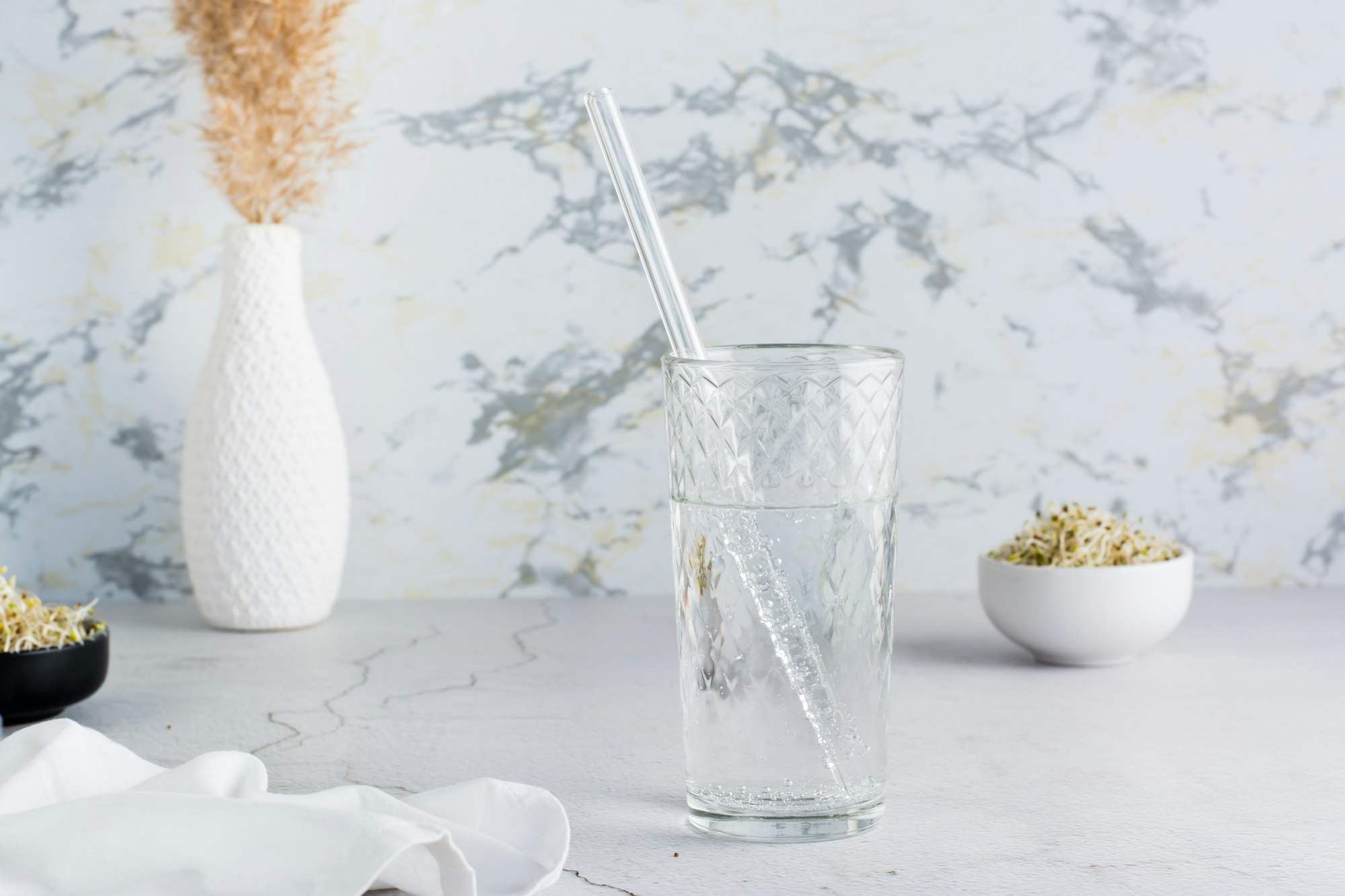 A glass of clean water and a glass straw for drinking on a light table.