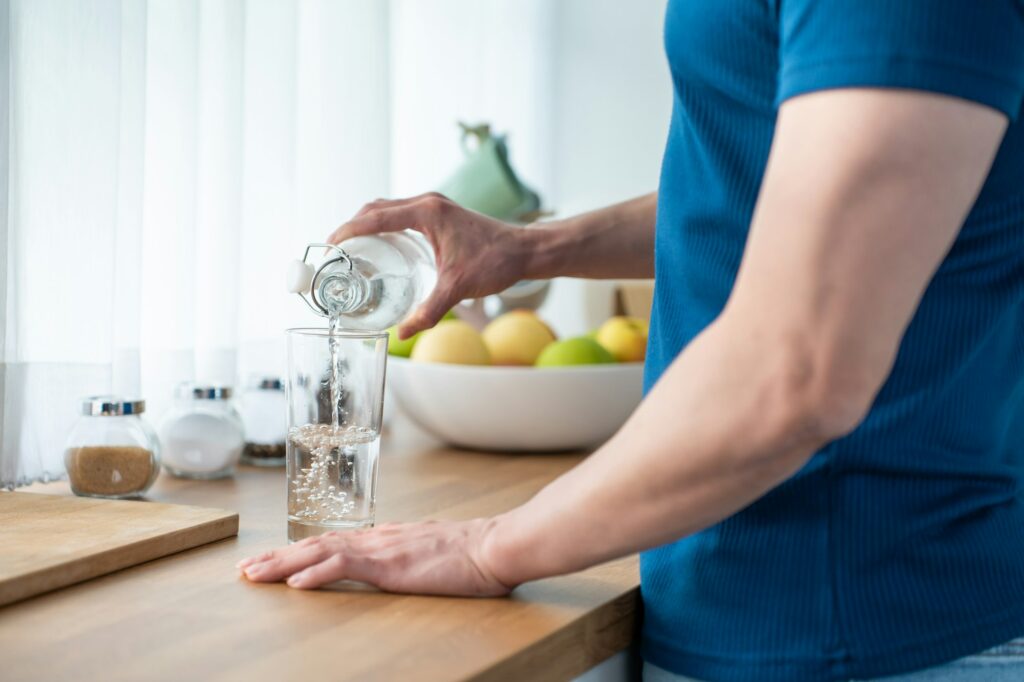 Close up hands of active strong man pouring clean water into glass.