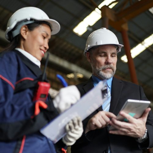 Factory manager and female engineer in factory and inspecting factory in industry plant background.
